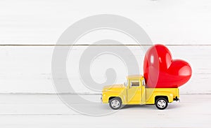 Red Heart on Toy Yellow Pickup Car on white wood background. Travel Love Concept with Copy Space