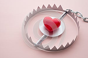 Red heart in a trap on pink background. Online internet romance scam concept. Love is bait or victim
