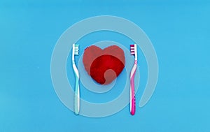 Red heart between two toothbrushes on pastel blue pink background. Male and female teeth hygiene concept. Close up. Empty place