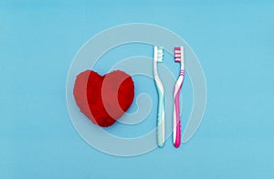 Red heart between two toothbrushes on pastel blue pink background. Male and female teeth hygiene concept. Close up. Empty place