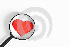 Red heart under a magnifying glass on a white background. Verification, confirmation and verification of love. Free space for an