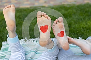 red hearts drawn on the bare feet of two children lying on the green grass