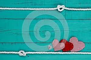 Red hearts and heart lock by rope border against teal blue wooden background