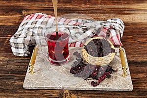 Red hibiscus tea in glass cup on white wooden table with dry rose petals. Hibiscus tea background