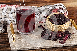 Red hibiscus tea in glass cup on white wooden table with dry rose petals. Hibiscus tea background