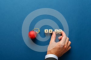 Red holiday bauble next to a 2019 sign on wooden dices with male hand changing it to 2020