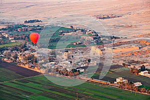 Red hot air balloon flying over the viiage in Theban Necropolis at Valley of The Kings