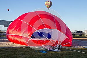 A red hot air balloon is on the ground being deflated.