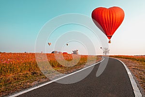 Red hot air balloon in heart shape over flower field. Symbol of love and valentines.