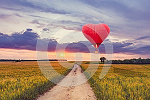 Red hot air balloon in the shape of a heart above the field