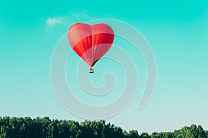 Red hot air balloon in the shape of a heart against the blue sky