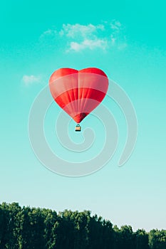 Red hot air balloon in the shape of a heart against the blue sky
