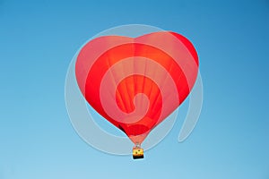 Red hot air balloon in the shape of a heart in clear blue sky. Aerostat over the field landscape