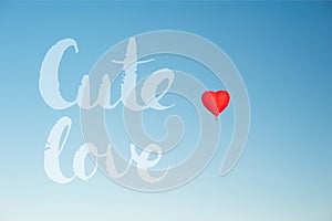 Red hot air balloon in the shape of a heart in clear blue sky. Cute love lettering words