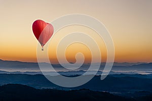 Red hot air balloon in the shape of a heart flying over the mountain