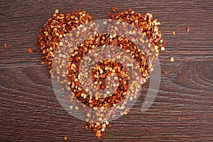 Red hot chili pepper flakes lying on wooden table in heart shape. Cooking concept, seasonings for food.