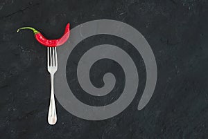 Red hot chili pepper on vintage silver fork over black slate stone background, top view.