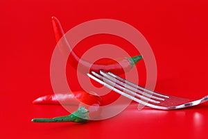 Red hot chili pepper on vintage silver fork over red background