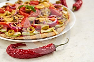 Red hot chili pepper on white surface close up. On blurred background vegetarian pizza with tomatoes, bell pepper, onion