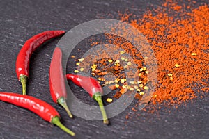 Red hot Chili peppers, red pepper flakes and chilli powder on black background