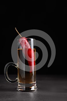 Red hot chili peppers and vodka in shot glass on grey table against black background