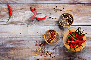 Red hot chilli pepper pods in a wooden mortar, pepper flakes and peppercorns in wooden bowls