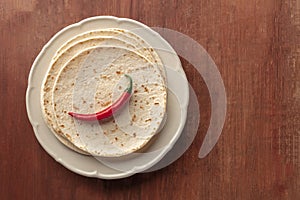 A red hot chilli pepper, shot from above on a pile of tortillas, Mexican flatbreads, on a dark rustic wooden background