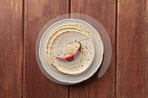 A red hot chilli pepper, shot from the top on a pile of tortillas, Mexican flatbreads, on a dark rustic wooden background