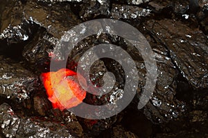 Red hot coal bar in focus on other cold raw bars of coal. Background of raw coal nuggets with soft focus