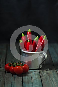 Red hot peppers in an aluminum mug on the table, tomato