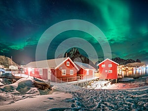 Red house in fishing village with aurora borealis over arctic ocean in winter at night