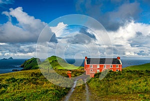 A red house in the Ireland countryside contrasting with the cloudy sky and the grren fiends