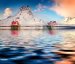 Red houses and huge snowy peaks reflected in calm waters of Hovdanvika Flord.