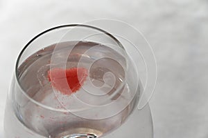 A red ice cube is melting into the clear liquid in the glass