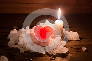 Red ice heart and the burning candle on a hill of white snow