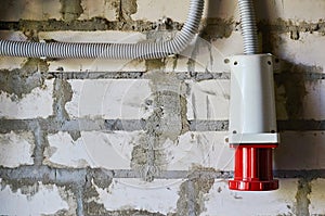 Red industrial connector for electrical appliances located on a brick wall.