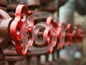 Red industrial valves in a row on petrochemical plant pipelines system selective focus over out of focus background