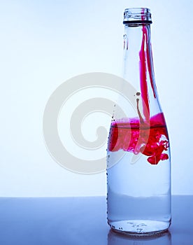 Red ink mixed with water in a glass bottle on a light background