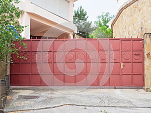 A red iron fence with a wicket gate, geometric pattern and sharp spiers encloses a modern residential building and a