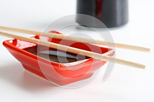 Red Japanese sauce bowl - seyuzaru, chopsticks and a bottle of soy sauce on a white kitchen table. Selective focusing. Daylight