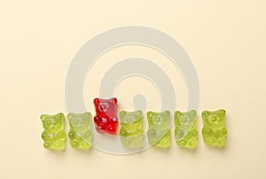 Red jelly bear among green ones on beige background, flat lay. Uniqueness concept