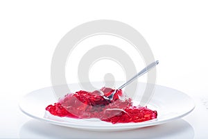 Red jelly in a white plate with a spoon. Eat jelly from a plate. Isolate