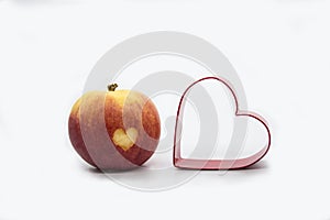 Red Juicy apple with a heart shape cut-out and heart shaped cookie cutter. Isolated on white background