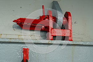 Red jumping stopper or securing cleat with chain used to secure movement of hatch covers of container ship while vessel is at sea.