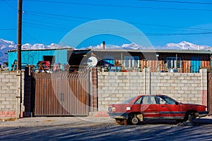 Red junked car without wheels in front of brick fence of junkyard, outside