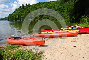 Red kayaks stretched out on the sandy shore of a calm lake surrounded by forest hills photo