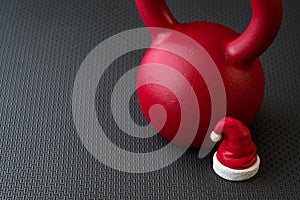 Red kettlebell on a black gym floor with small red and white Santa Claus hat