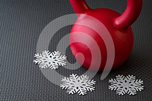 Red kettlebell on a black gym floor with three silver snowflakes