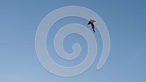 A red kite flying in the air against the background of a blue summer sky.