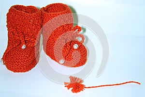 Red knitted baby booties and a red pompon of yarn on a white background